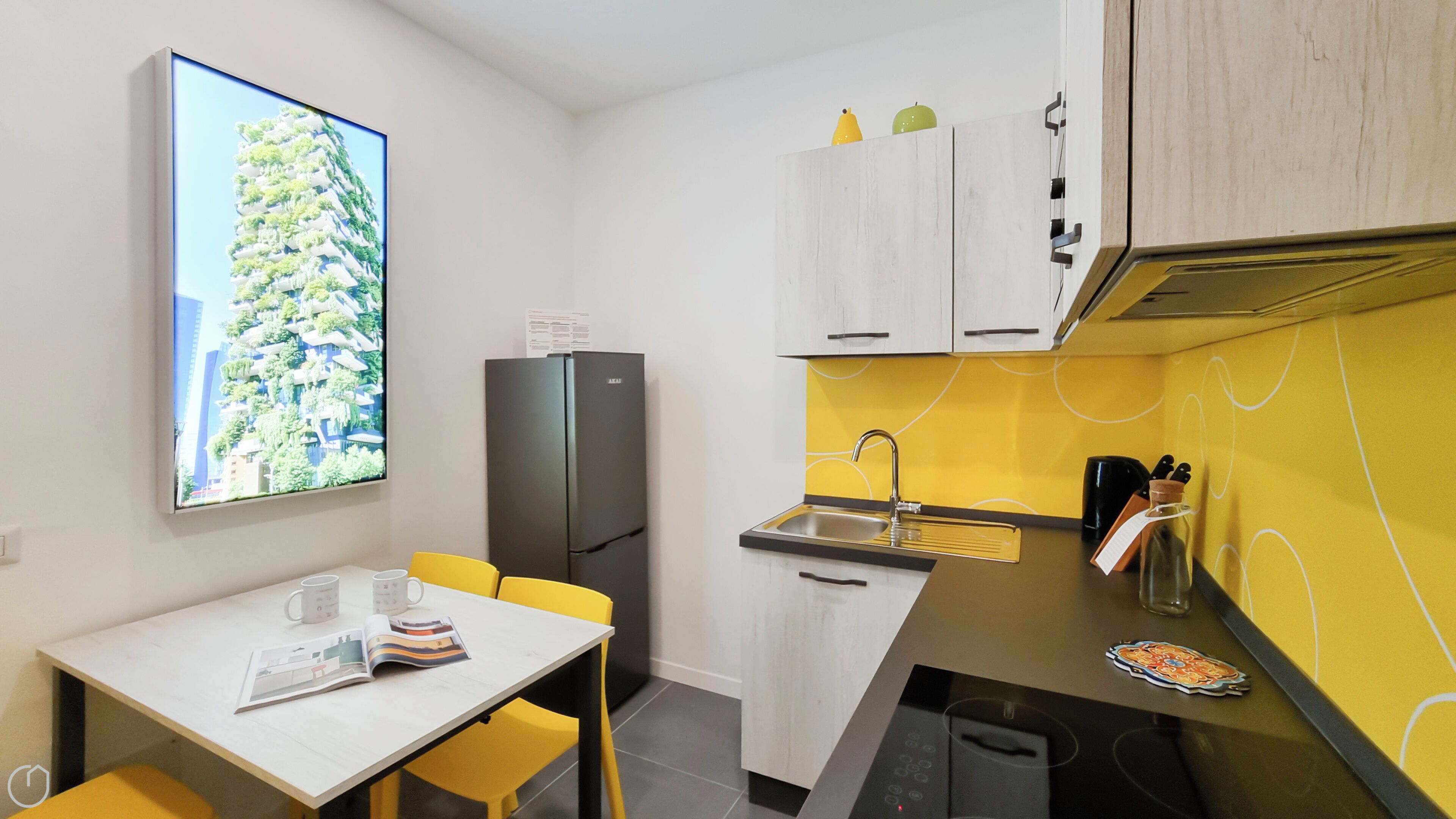 Cocina compacta con refrigerador, lavamanos y comedor con sillas amarillas.