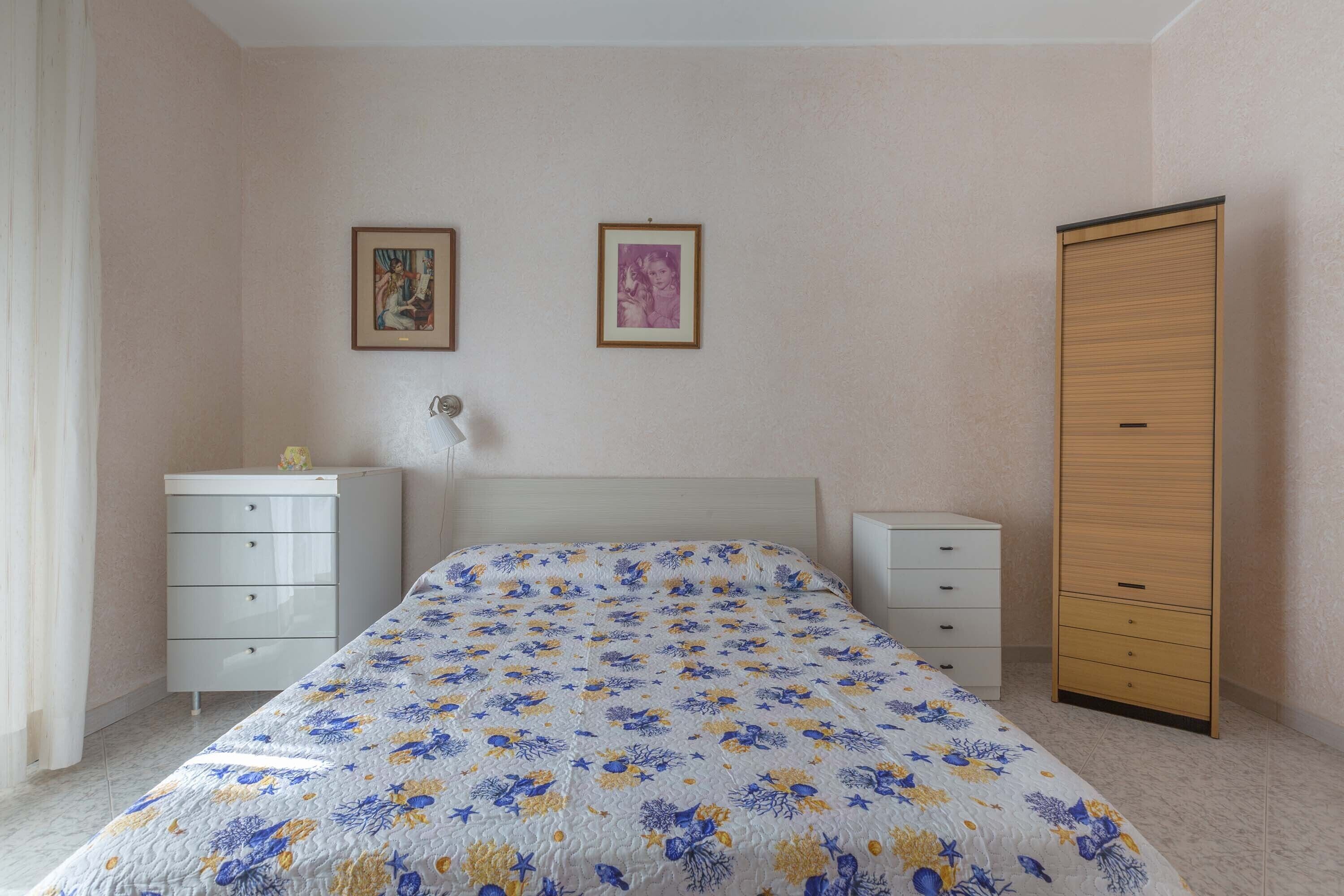 A bedroom with a bed, two bedside tables, a wardrobe, and two framed pictures on the wall.