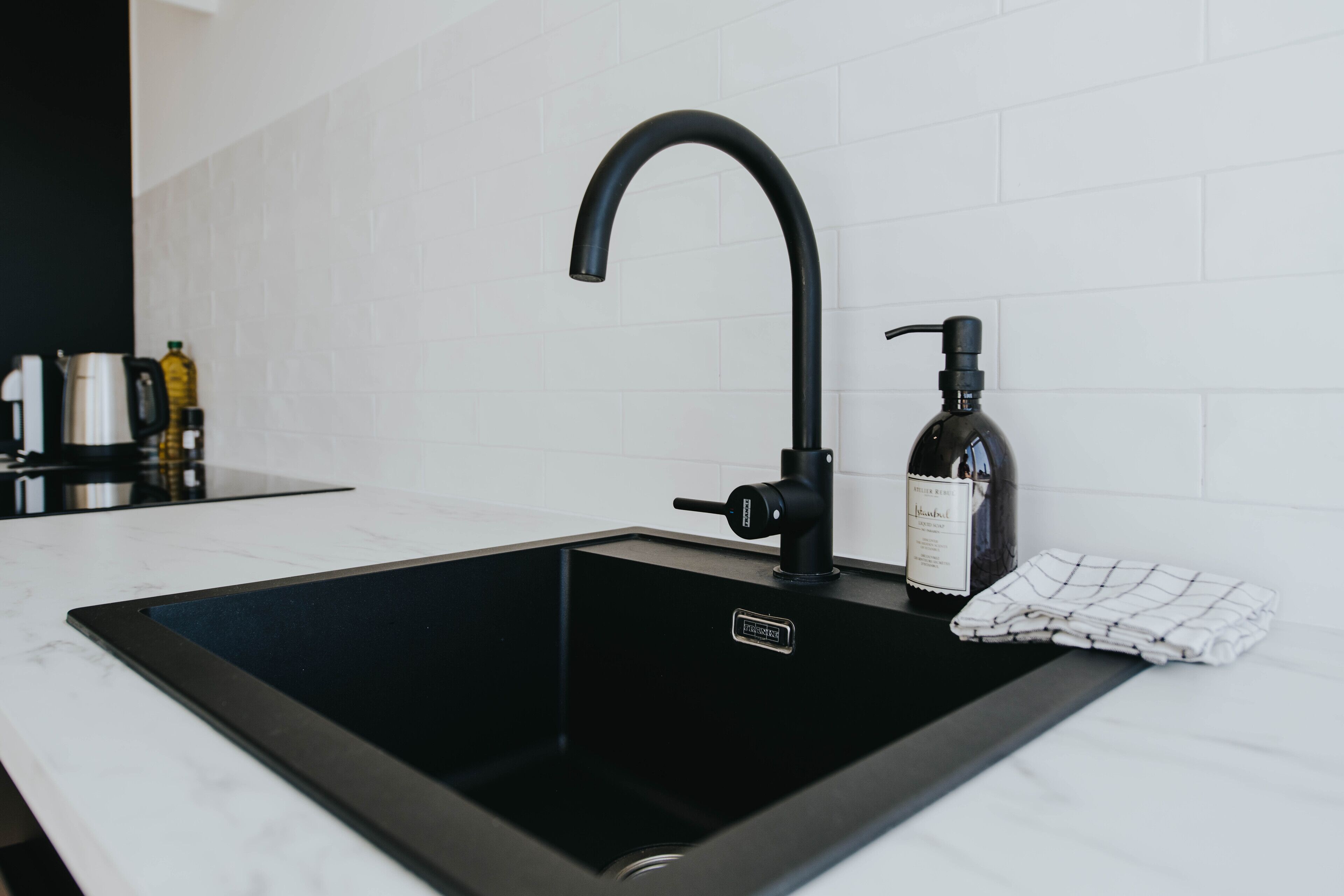 Una cucina moderna con un lavello nero, una bottiglia di vino e un panno ripiegato sul piano di lavoro.