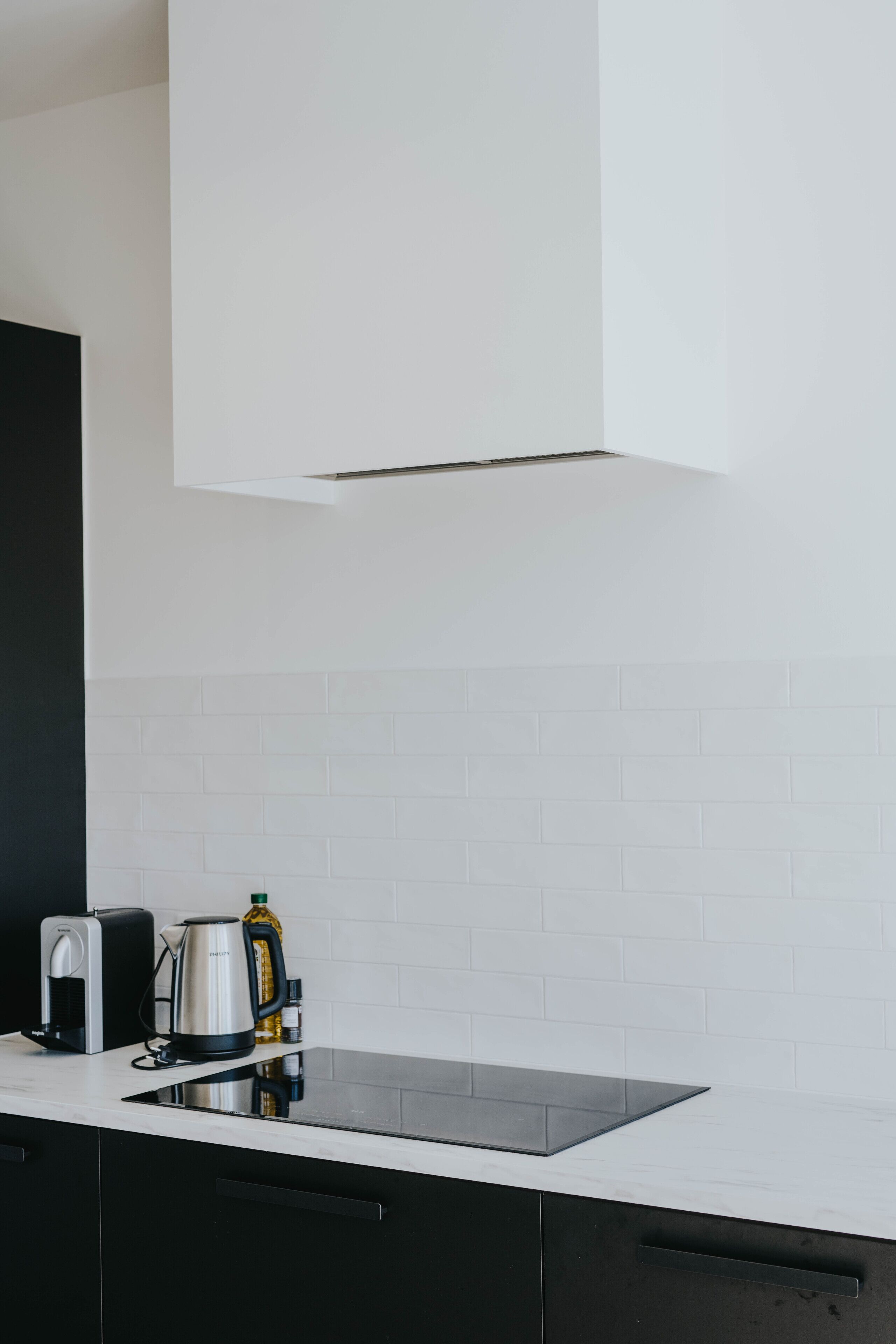 A modern kitchen with a white tiled backsplash, a black countertop, and a stainless steel kettle.