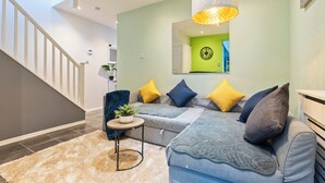 Una sala moderna con una escalera, un conjunto de sofás, una mesita con una planta y una lámpara colgante grande.