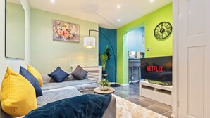 Una sala moderna con un sofá, cojines, una mesa de centro, una planta, un televisor y un reloj en la pared.