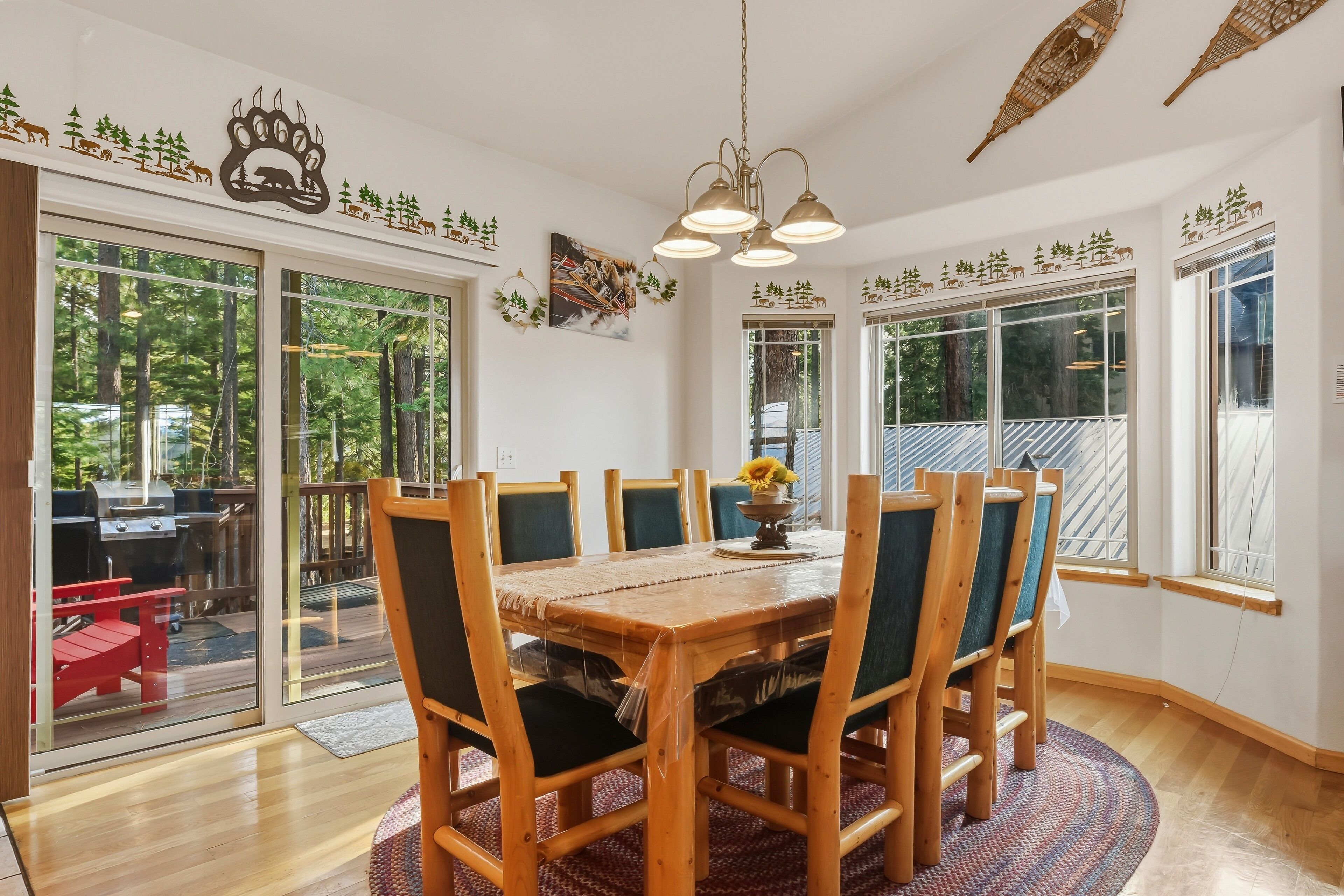 Un espace repas comprenant une table et des chaises en bois, un lustre et de grandes fenêtres donnant sur l’extérieur.