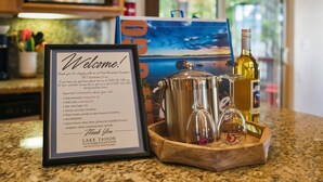 A framed welcome sign with contact information and amenities, a stainless steel pot, a wine bottle, and a glass on a wooden tray on a kitchen counter. - Pine Mountain Paradise 3 Bedroom Home by RedAwning (South Lake Tahoe)
