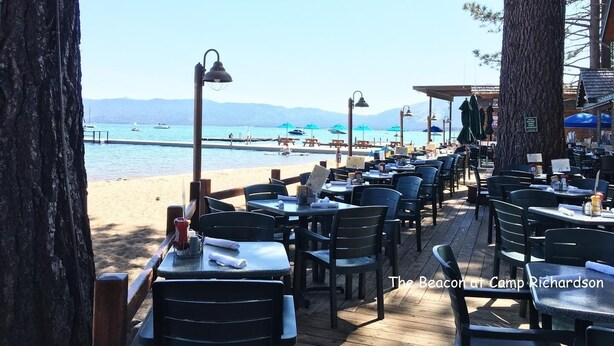 An outdoor dining area with tables and chairs, overlooking a beach and the sea.