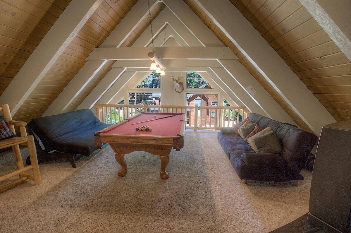 An attic room with a pool table, a sofa, and a television.