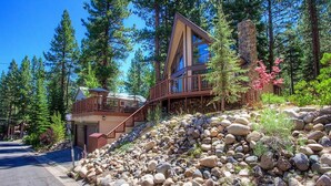A modern lodge with a stone facade, wooden deck, and a staircase leading to a second level.
