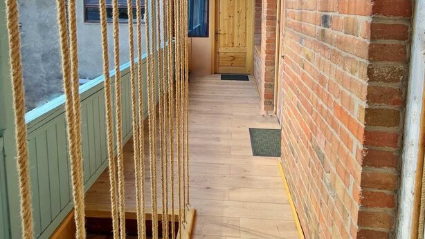 A narrow hallway with a wooden floor, a brick wall, and a wooden door at the end. - ApartTen (Tbilisi)