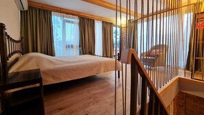A bedroom with a wooden bed, a wooden desk, a window with curtains, and a staircase with a railing. - ApartTen (Tbilisi)