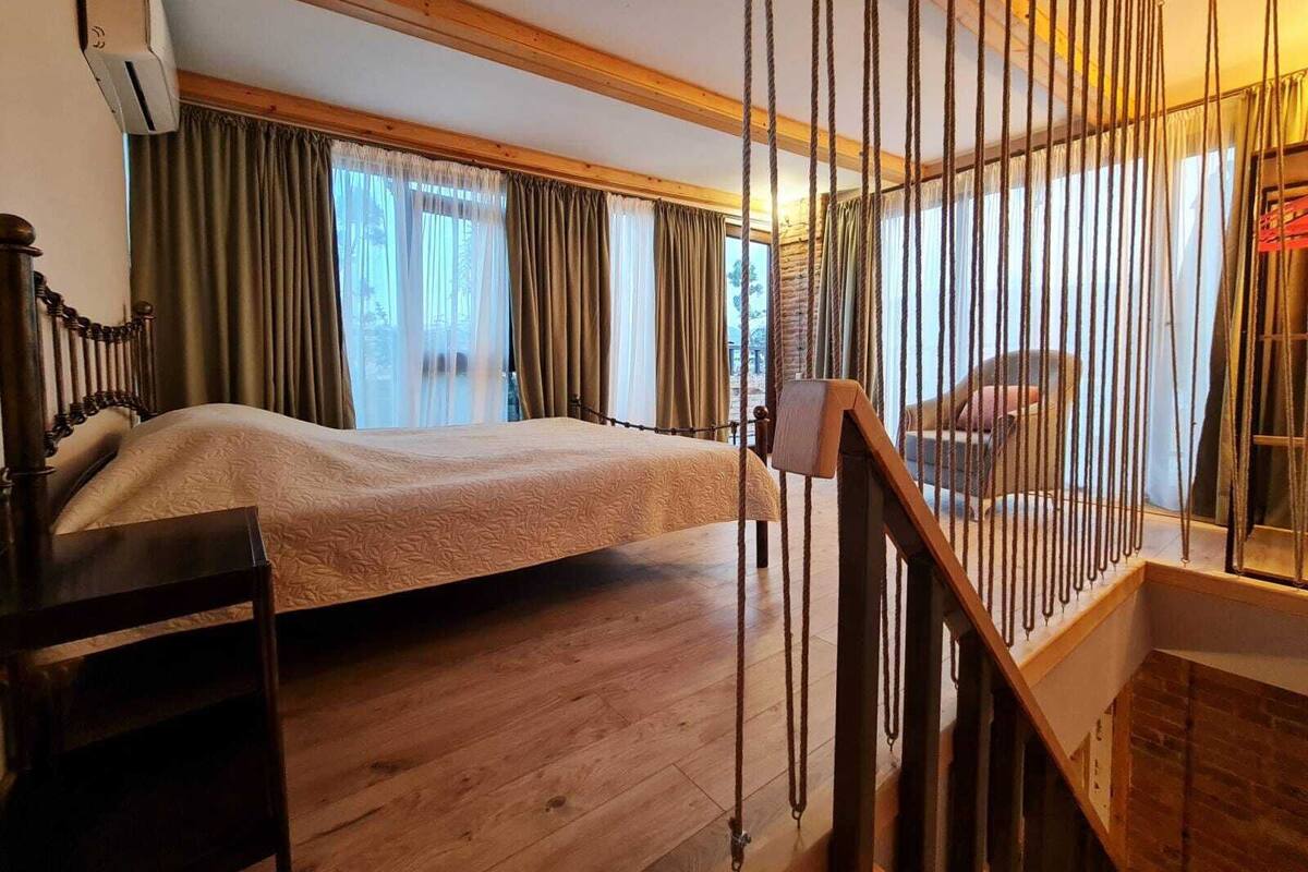 Une chambre à coucher avec un lit en bois, un bureau en bois, une fenêtre avec des rideaux et un escalier doté d’une rampe.