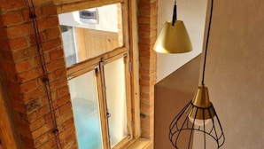 A room with exposed brick walls, a large window, and a hanging pendant light. - ApartTen (Tbilisi)