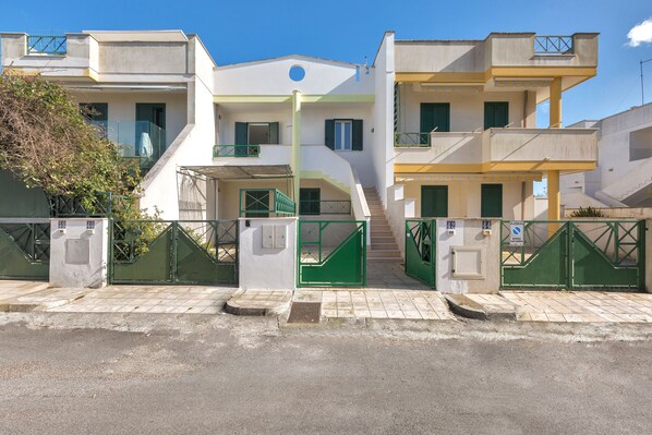 A multi-story residential building with a central staircase, green shutters, and a gated entrance.