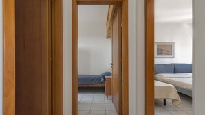A narrow hallway with wooden doors leading to a bedroom with a bed and a window.