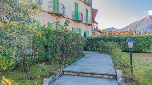 A pathway leading to a building with balconies and green shutters. - Green Rose by Wonderful Italy (Bellagio)