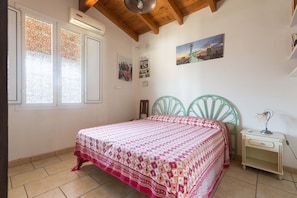 Un dormitorio con una cama, una mesita de noche, cabecera de metal verde, una ventana con vidrio esmerilado y una pared con cuadros enmarcados.