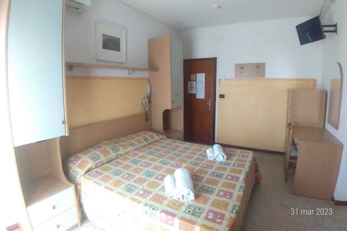 A hotel room with a bed, a wardrobe, a desk, and a chair.