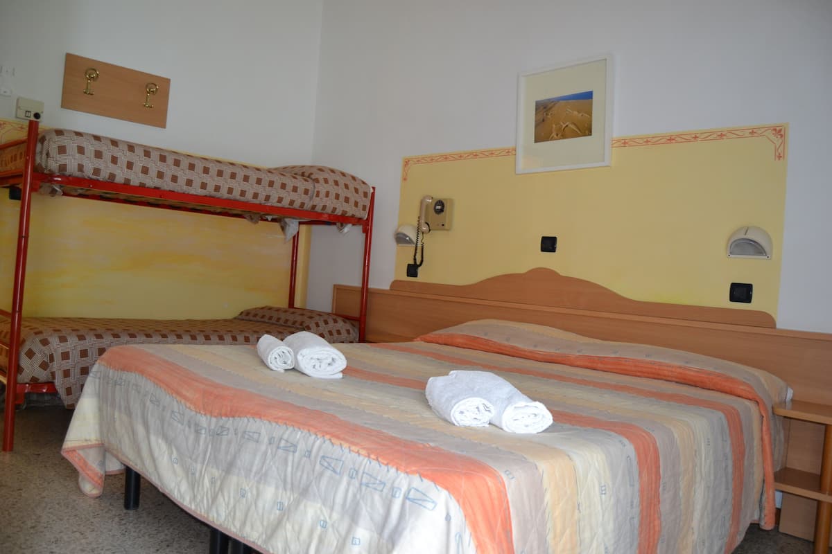 A room with two bunk beds, a single bed with rolled towels, a telephone, and a framed picture on the wall.
