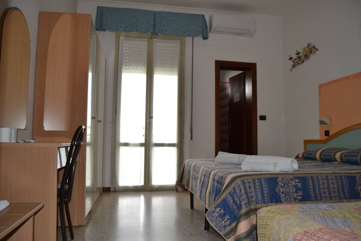 A bedroom with a bed, a desk, and a chair. There is a door leading to another room.