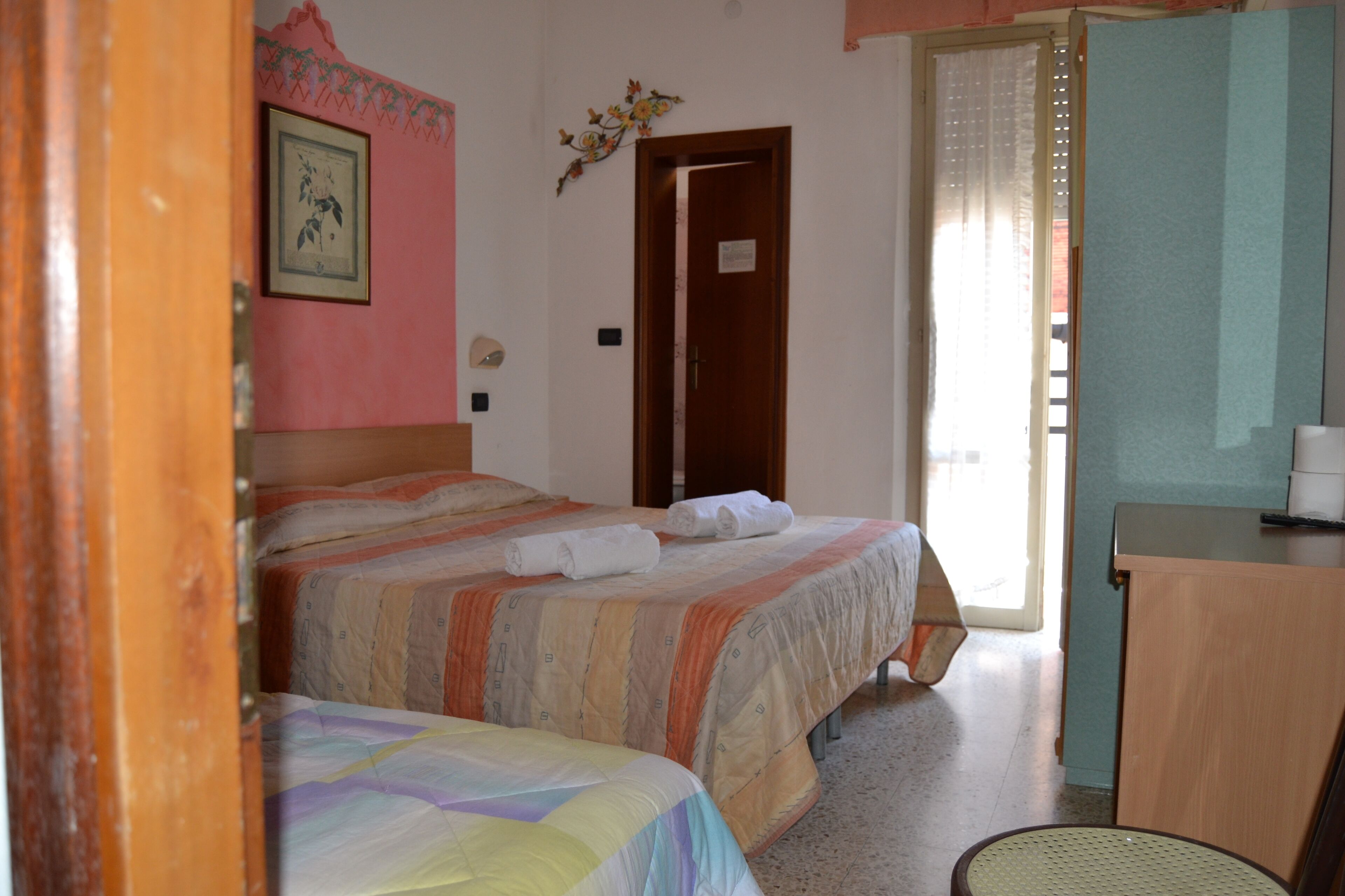 A hotel room with two beds, a desk, a chair, a door, and a window with curtains.