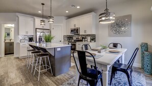 Uma cozinha moderna com armários brancos, eletrodomésticos de aço inoxidável e uma ilha central com banquetas.