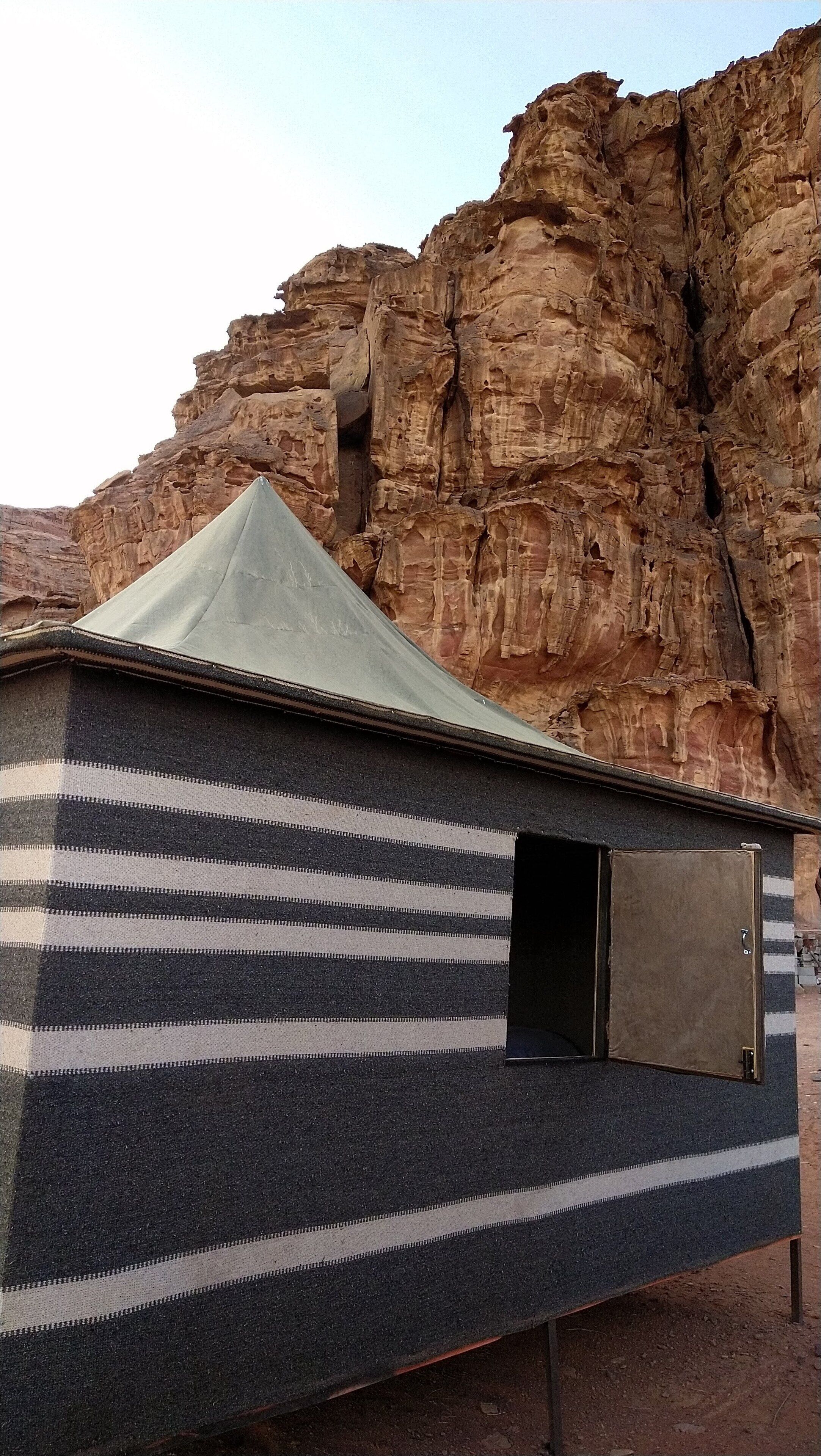 A small, striped tent-like structure with a metal door, set against a rocky cliff backdrop.