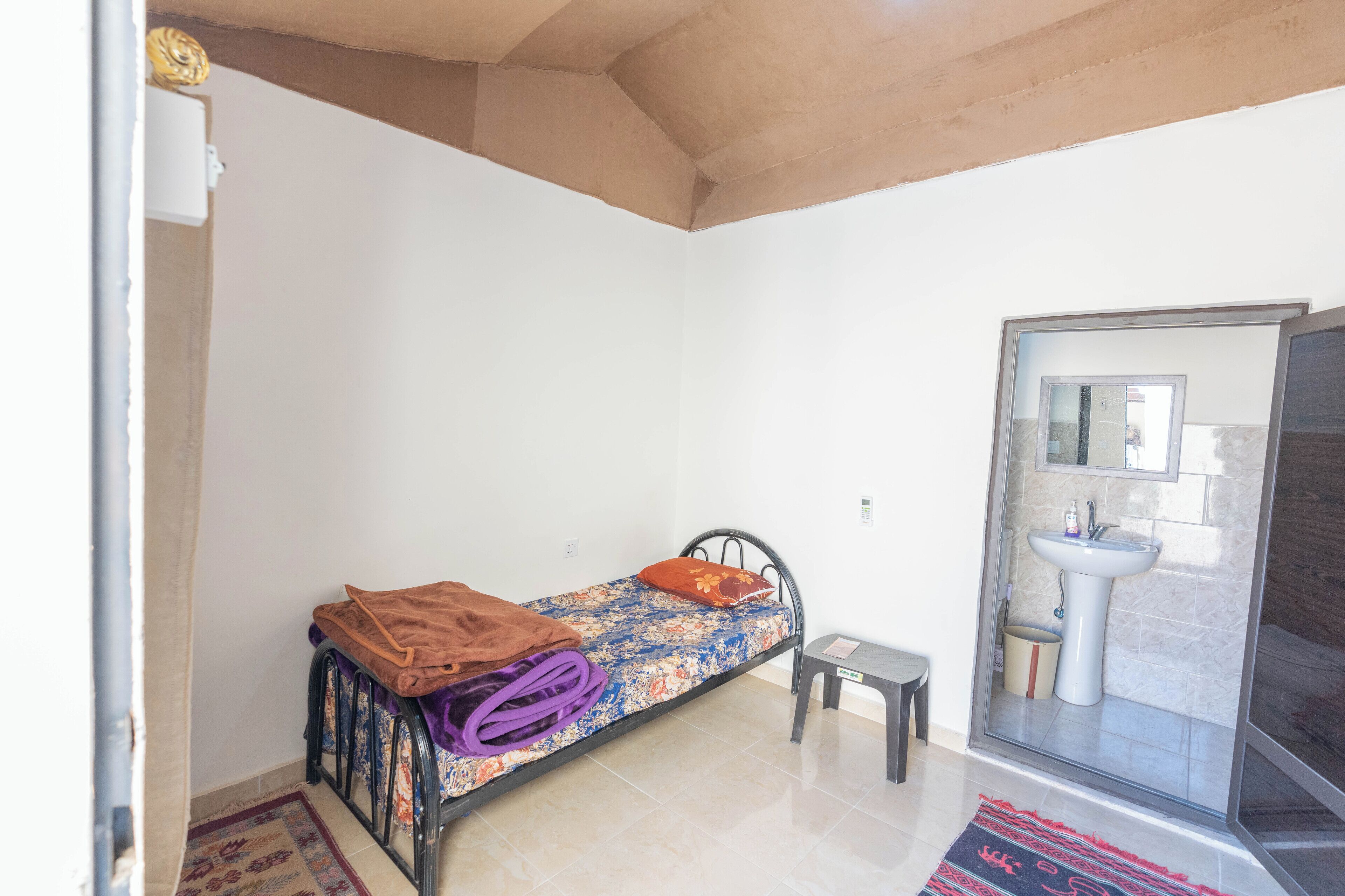 A small, single-bed room with a bathroom that includes a sink and a shower.