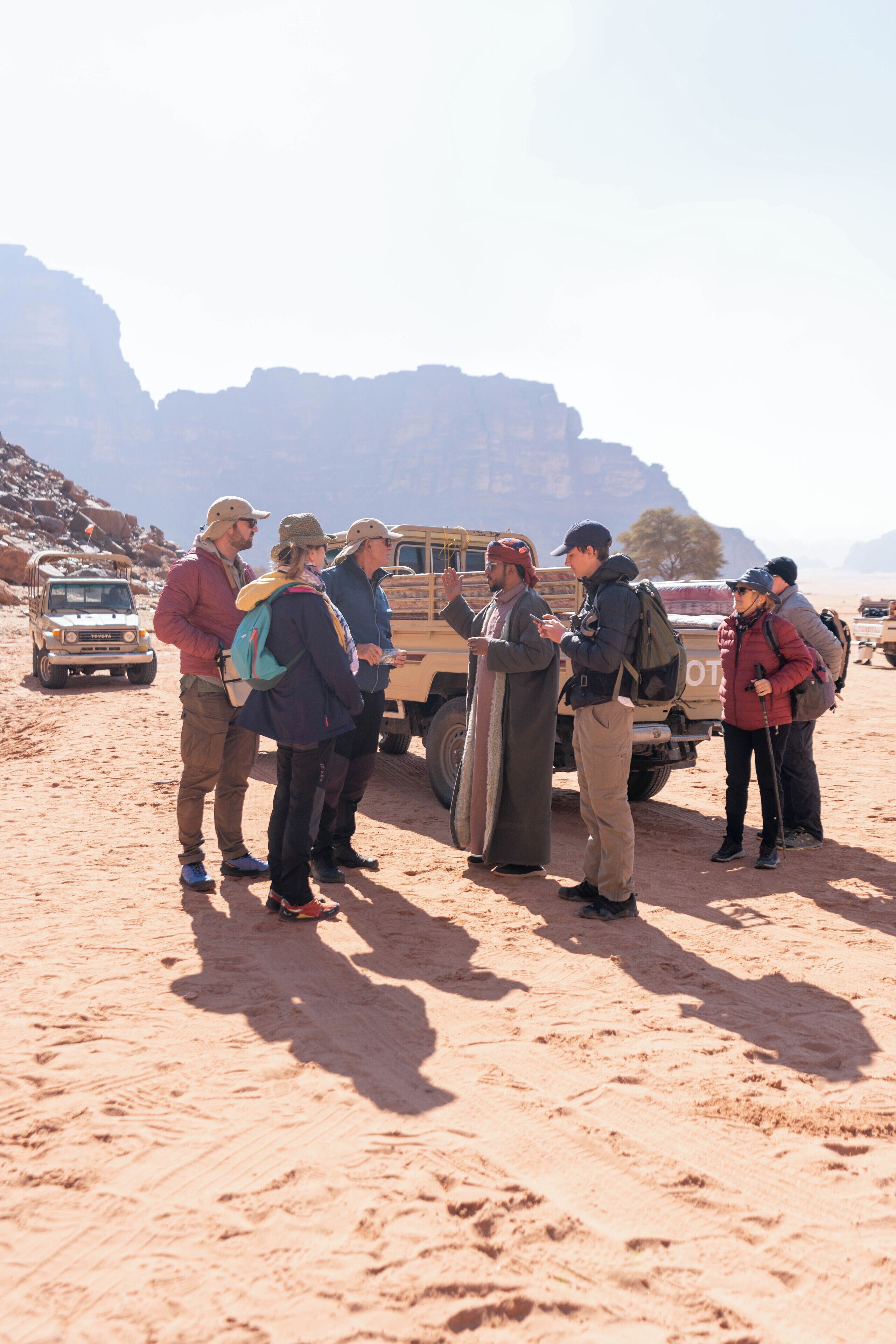 Un grupo de personas en un desierto, con un vehículo al fondo.