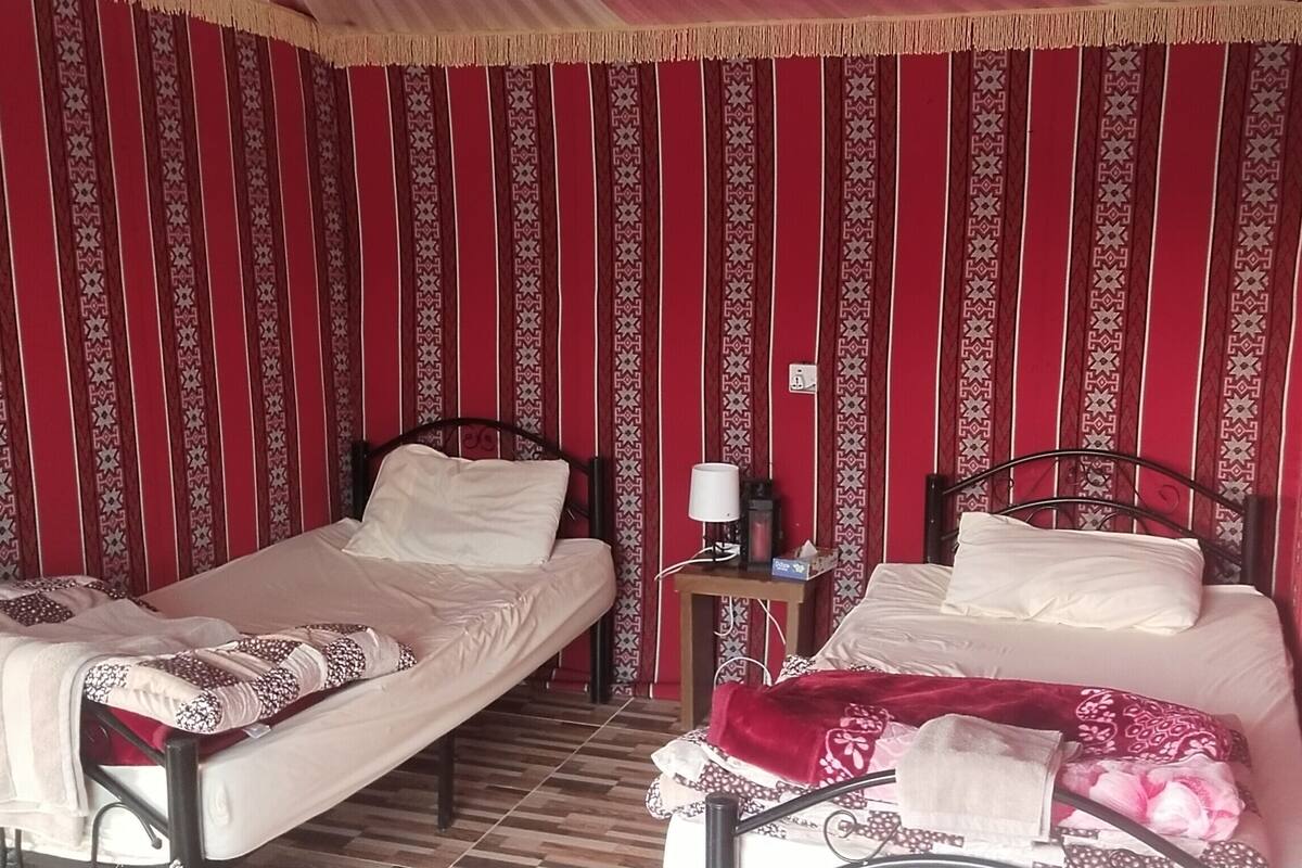 Quarto com duas camas, uma mesa de cabeceira e parede estampada.