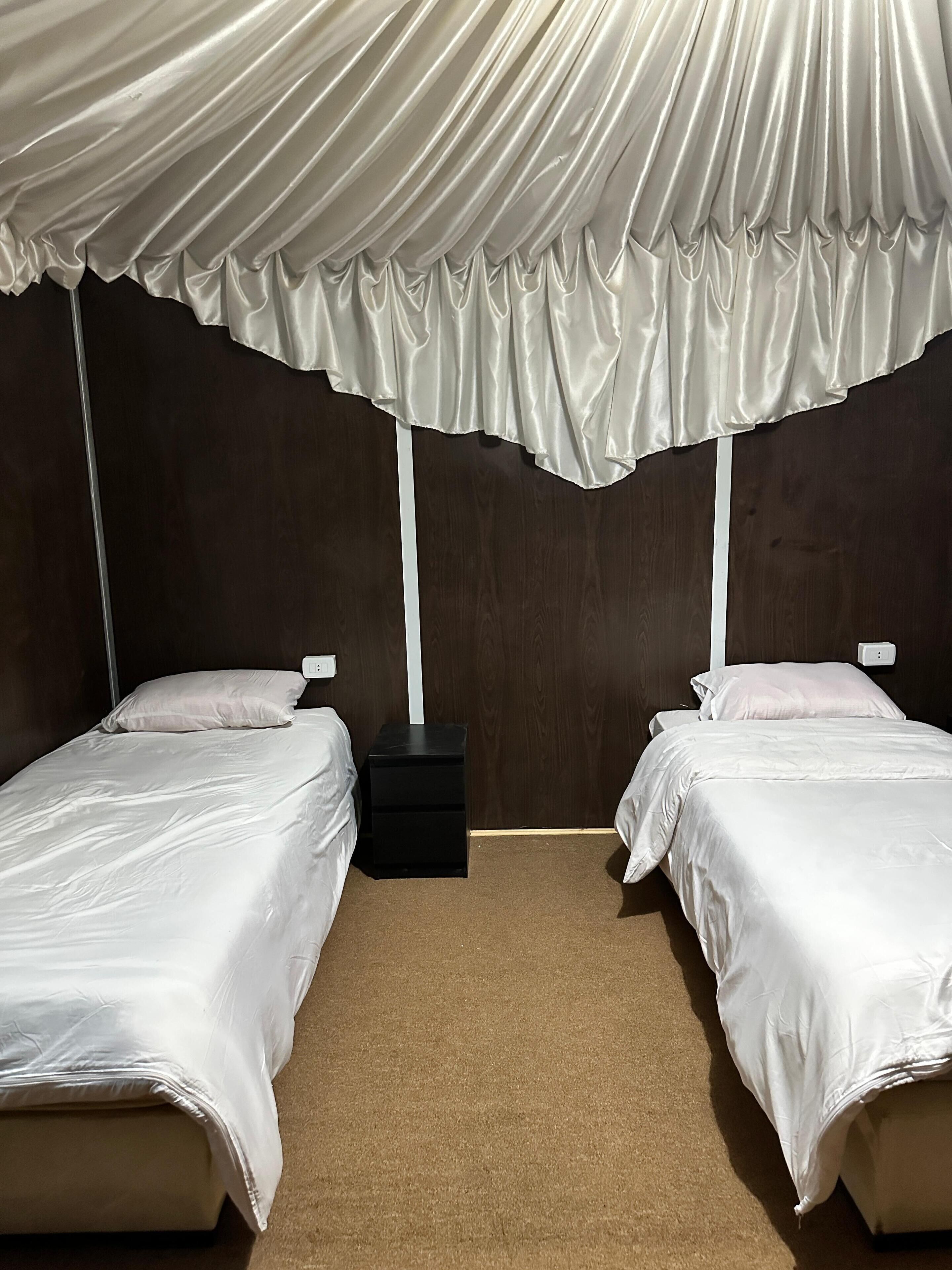 Ein Zimmer mit zwei Einzelbetten, einem kleinen schwarzen Nachttisch und einem weißen Baldachin über den Betten.