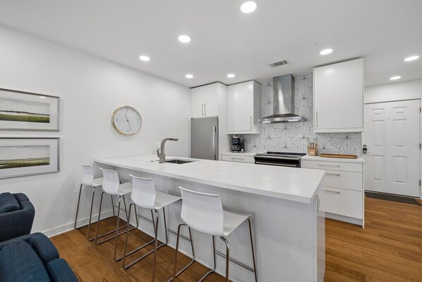 A modern kitchen with white cabinetry, a central island with bar stools, a stainless steel refrigerator, and a built-in oven. - Sleek Seagrove Studio on 30a- 2-Minute Walk to the Beach! (Santa Rosa Beach)