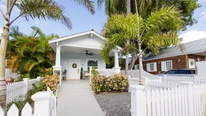 A white house with a covered porch, palm trees, and a white picket fence. - The Sandy Beach House in Historic Key West (Key West)