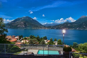 Vista de um lago com montanhas ao fundo, piscina e varanda com corrimão.