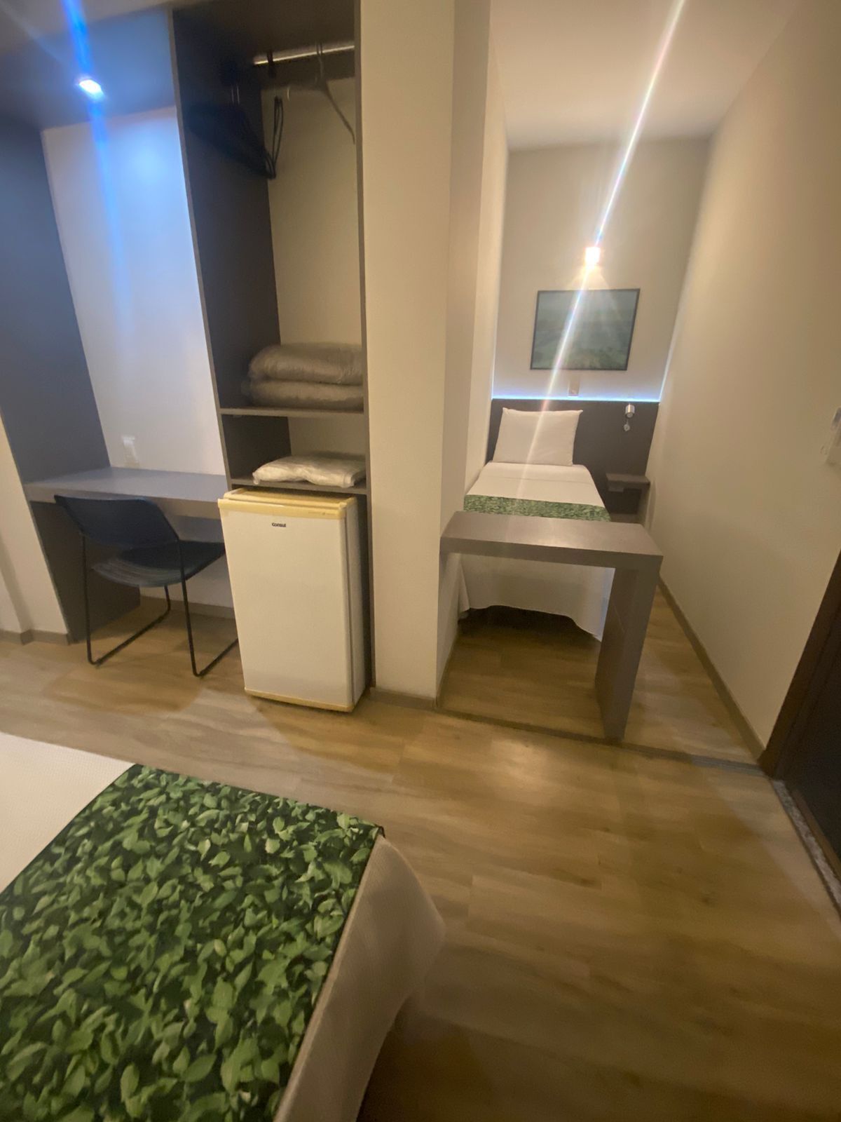 Una habitación de hotel compacta con cama, escritorio, refrigerador y armario.