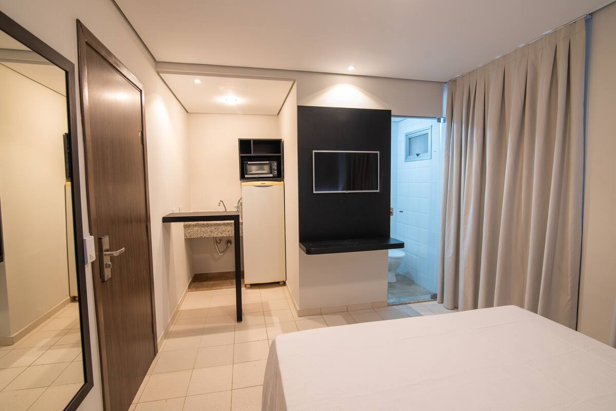 A modern hotel room with a bed, a small kitchenette, a TV, and a bathroom.