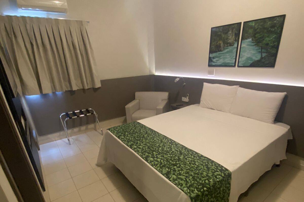 A hotel room with a bed, a chair, a desk, and a window with curtains.