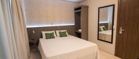 A bedroom with a bed, a mirror, a wardrobe, and a window with curtains.