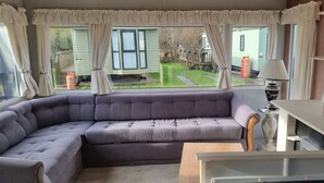 A corner sofa in a room with large windows, a lamp, and a view of a backyard. - Caravan - Sleeps 8, pet Friendly (Welshpool)