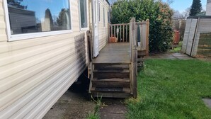 A mobile home with a wooden deck leading to a front door. - Caravan - Sleeps 8, pet Friendly (Welshpool)