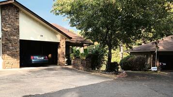 Un garage attenant à une maison, avec une façade en pierre, une voiture garée et un arbre dans l’allée.