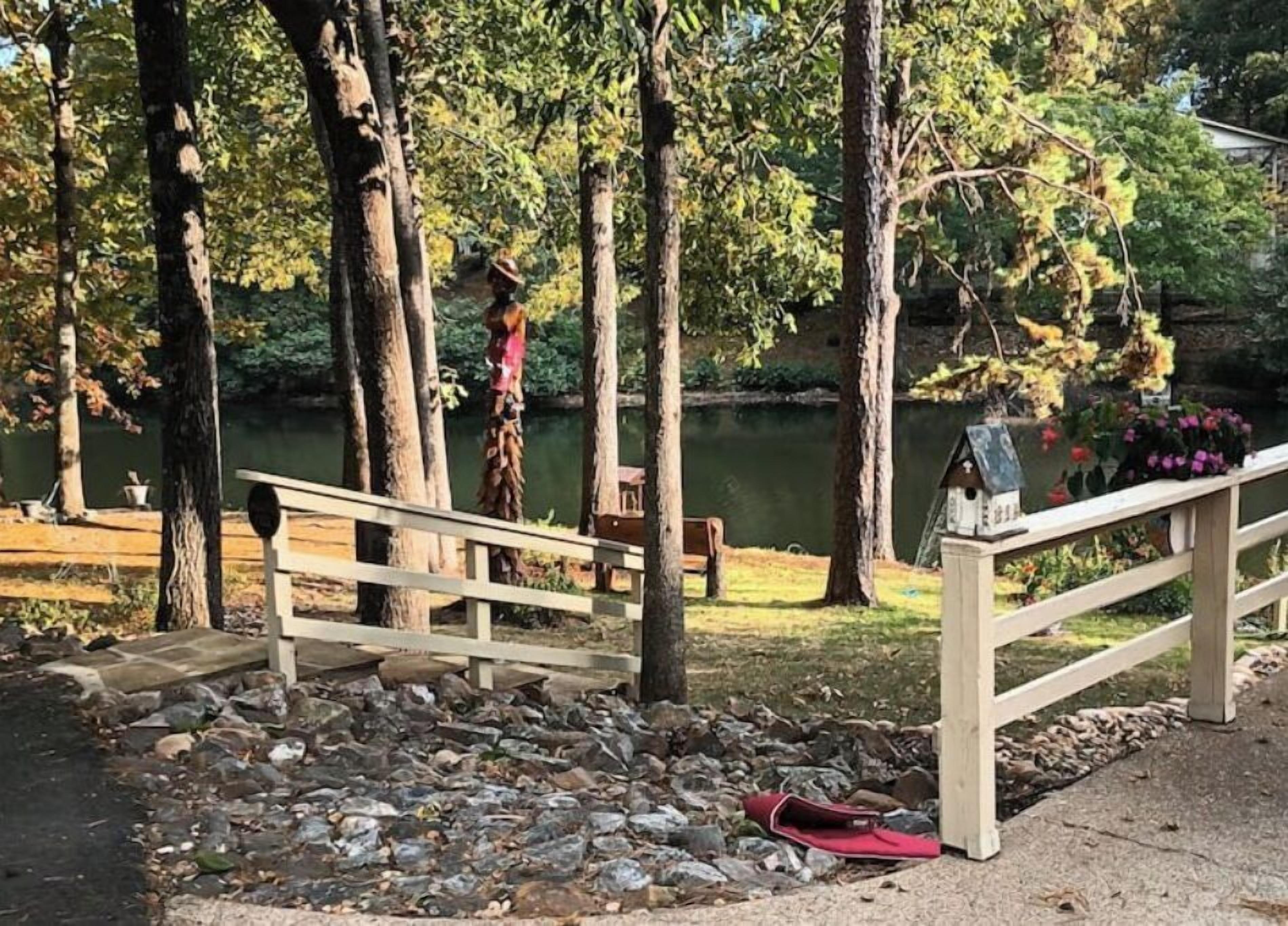 Un pont en bois enjambant une zone rocheuse, avec un banc et une nichoir à oiseaux sur la droite.