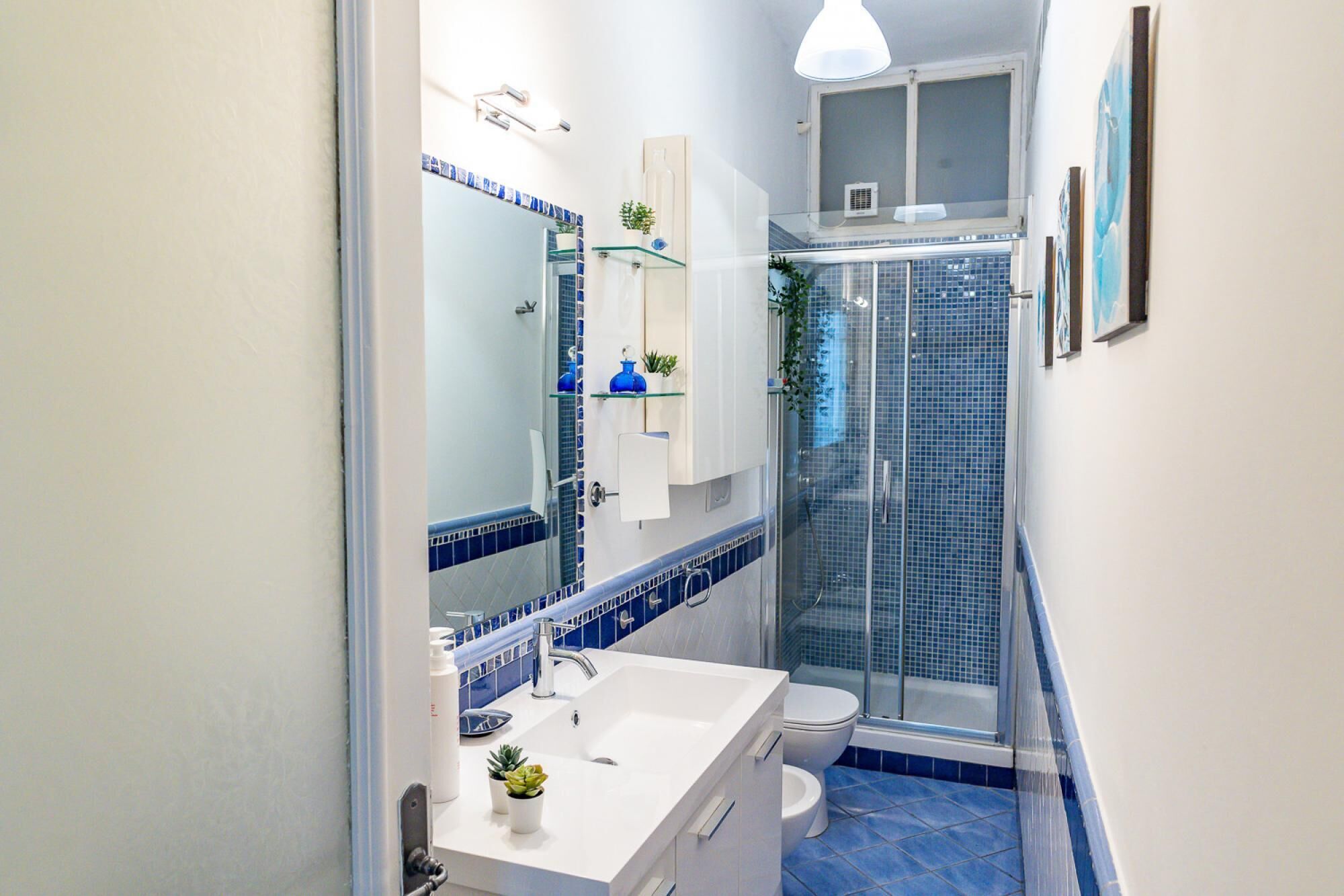 A bathroom with a white sink, blue-tiled shower, and a glass-enclosed shower stall.
