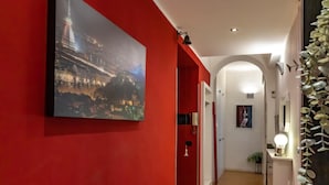 Ein Flur mit roter Wand, einem Stadtbild im Bilderrahmen, einer weißen Tür und einer kleinen Pflanze.