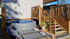 Un área moderna de hidromasaje al aire libre con una terraza de madera, una pequeña escalera y un espacio de estar cubierto.