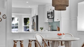 Una cocina moderna con armarios blancos, electrodomésticos de acero inoxidable y una mesa redonda con sillas de mimbre.
