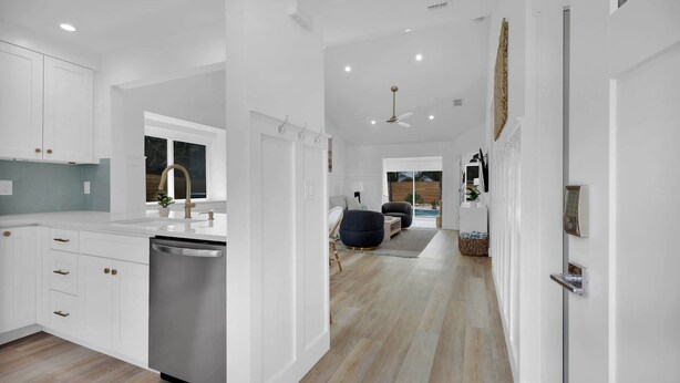 Una cocina moderna con armarios blancos, lavavajillas y un comedor con mesa y sillas.