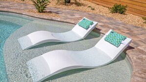 Una piscina con dos sillas de descanso blancas, cada una con un cojín estampado en verde.