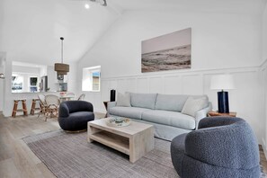 A modern living room with a light grey sofa, dark armchairs, a wooden coffee table, and a hanging light fixture. - The Blue Oasis - 3/2 POOL Home S Jax Beach (Jacksonville Beach)