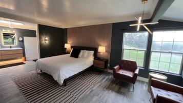 Une chambre moderne avec un grand lit, des lampes de chevet, un plancher en bois, un fauteuil rouge et une vue sur l’extérieur grâce à une grande fenêtre.