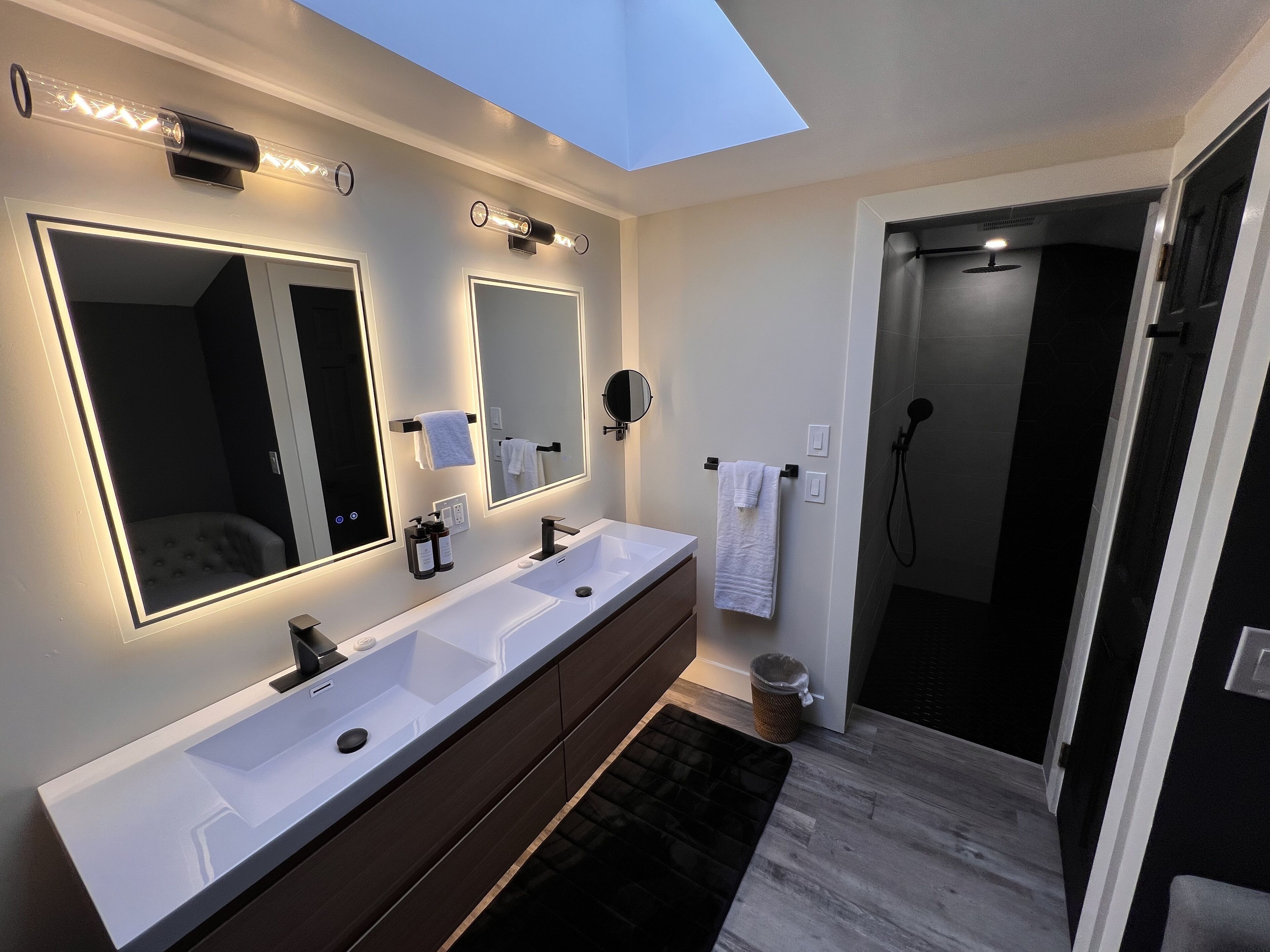 Ein modernes Badezimmer mit Oberlicht, zwei Waschbecken, einem großen Spiegel und einer Duschkabine.