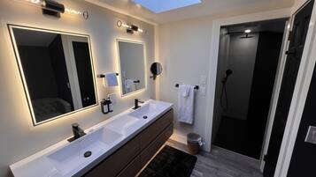 Ein modernes Badezimmer mit Oberlicht, zwei Waschbecken, einem großen Spiegel und einer Duschkabine.